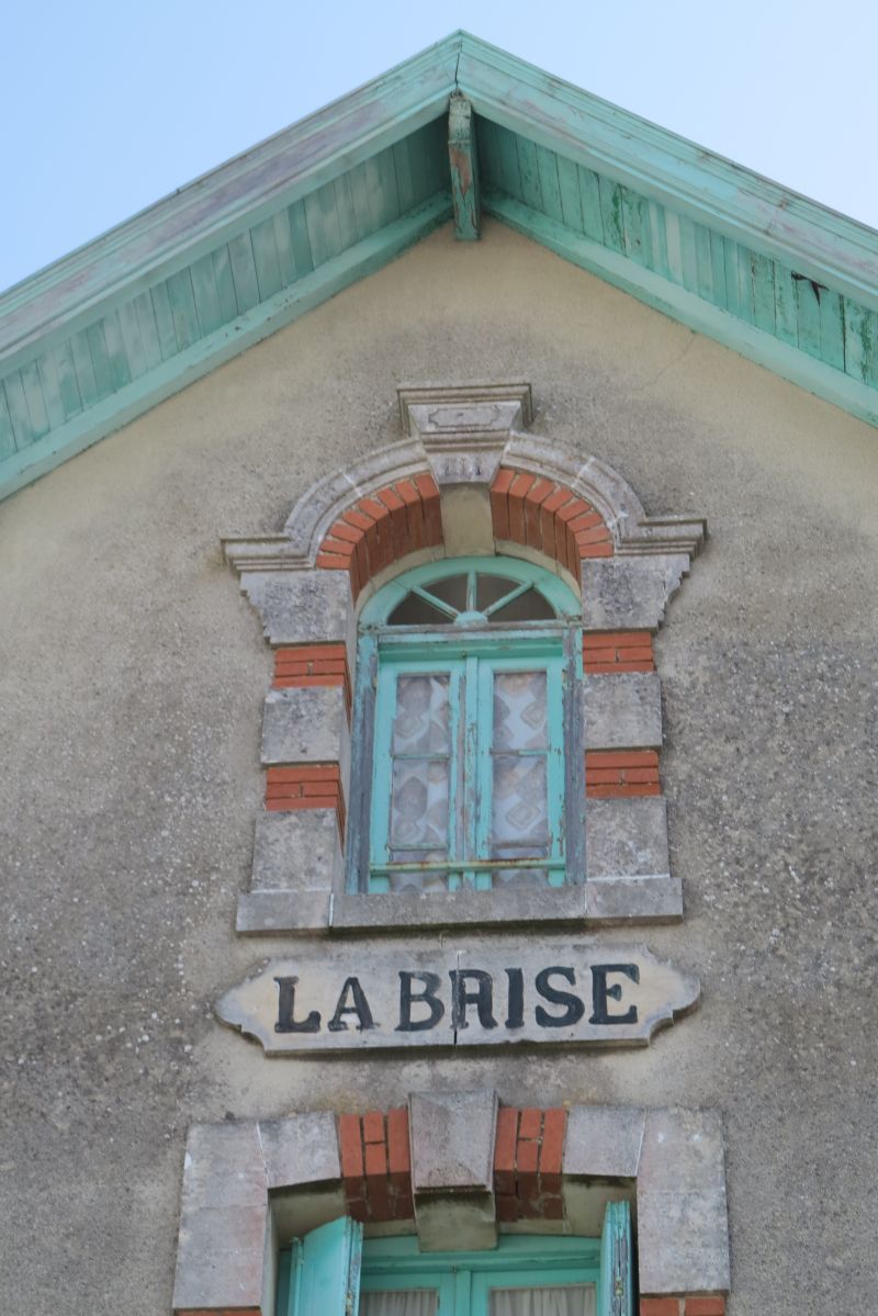 Détail de la façade : débordement de toit, fenêtre en plein cintre, cartouche et décor de brique et de pierre.