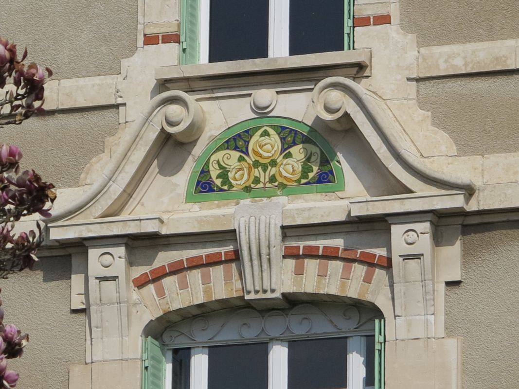 Détail du décor de l'avant-corps : fronton brisé, décor de roses en faïence, incrustations de brique rouge.