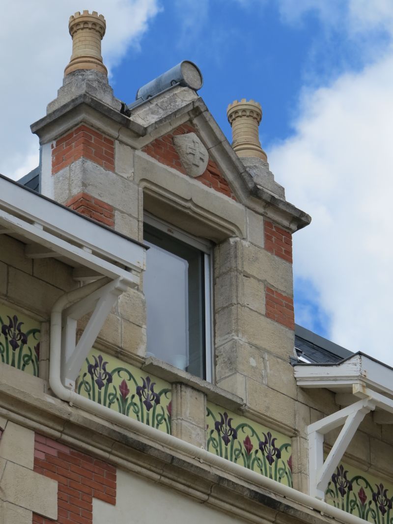 Lucarne en brique et pierre sur le côté droit de l'avant-corps côté boulevard : amortissements en forme de tours, écusson armorié, frise Art Nouveau.