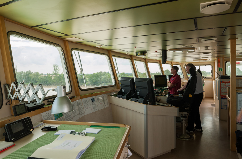 Vue intérieure de la cabine de pilotage : capitaine du bateau accompagné du pilote dans la remontée de l'estuaire.